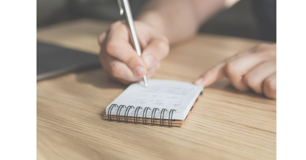 ノートにメモを取る手元が柔らかい光に照らされている